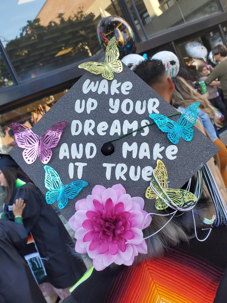 A graduation cap with the words Wake up your dreams and make it true glued on the top, along with paper butterflies and a flower