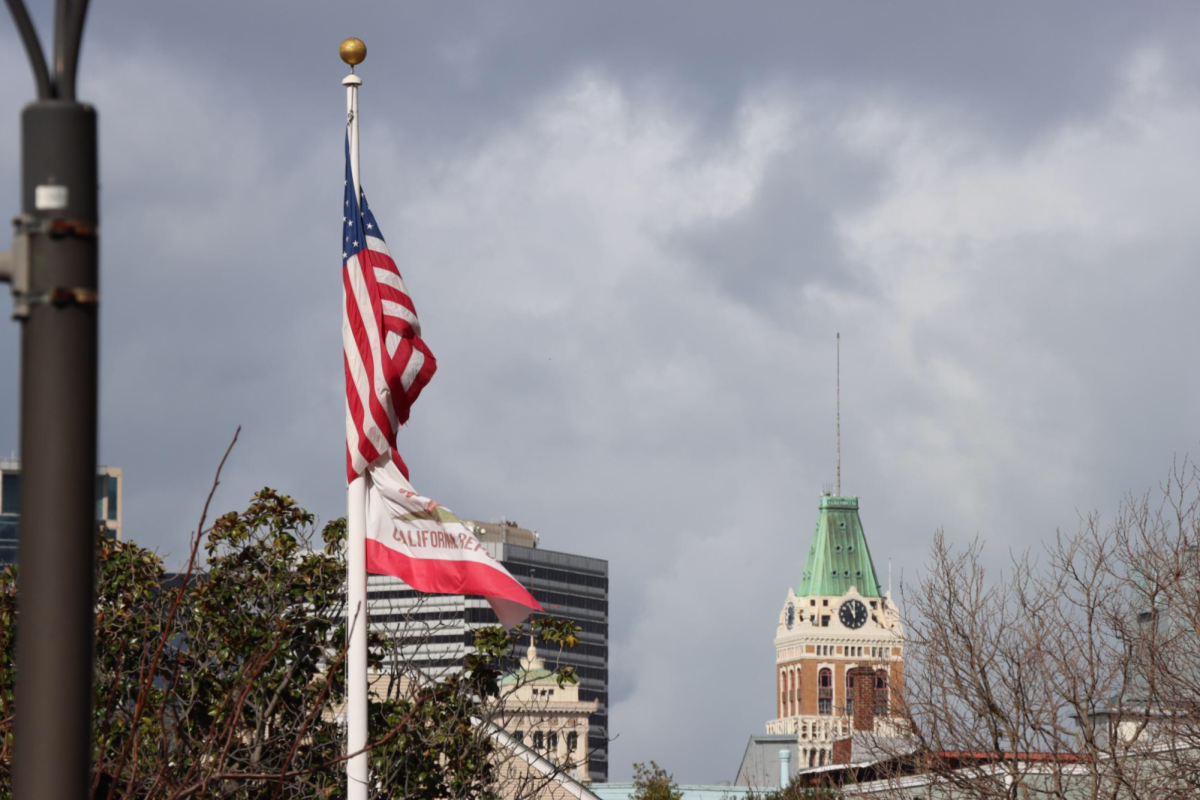 The state flag of California flies underneath the American flag on the west side of the Laney College campus. Behind, the Tribune Tower, which once housed Oaklands daily print newspaper, sits in the city skyline. Both California and the United States have open government laws that establish the publics right to information, but the Peralta Community College District consistently lags behind in comprehensively fulfilling requests for public information made by student journalists at The Citizen. (Photo: Li Khan/The Citizen)
