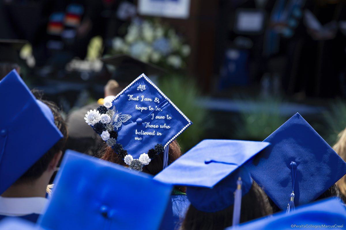 An audience in academic regalia watches a graduation ceremony. One graduation cap reads, "All that I am, & hope to be, I owe to those who believed in me[.]" (Photo: Marcus Creel/PCCD)