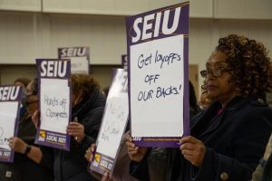 SEIU 1021 members carry protest signs decrying planned layoffs among Peralta employees. The district recently announced its intent to cut 68 positions across several departments, 44 of which are currently filled.