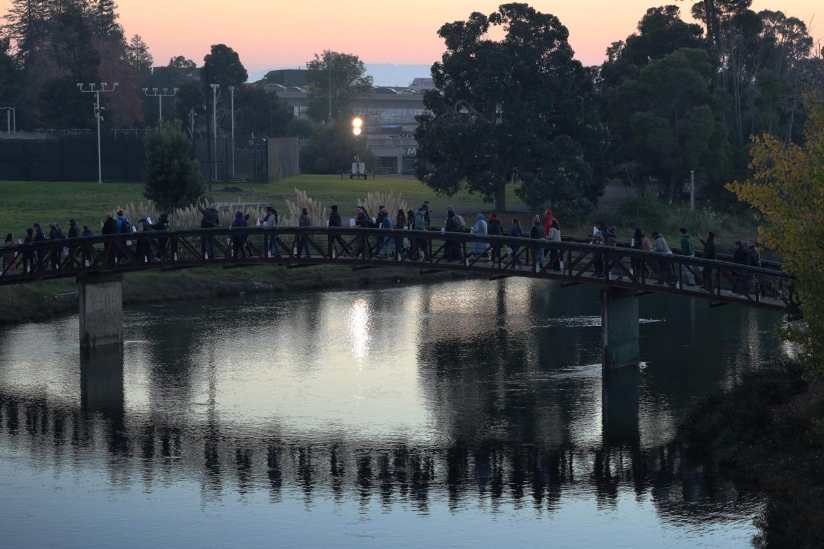 Mourners cross a bridge in the estuary at Laney College in Oakland, CA on Dec. 10, 2025. The "Light the Path, Light the Field" walk symbolically retraced a path John Beam and his students took between the college's main campus and its Fieldhouse building.